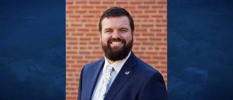 Photo of man in blazer smiling against brick wall