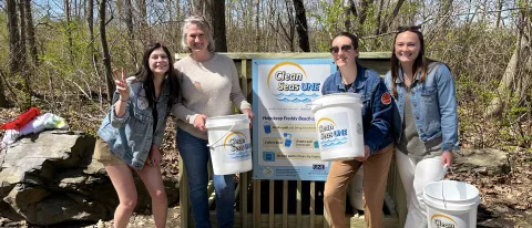 Students and a UNE staff member gather in front of the Clean Seas UNE beach cleanup kiosk at Freddy Beach