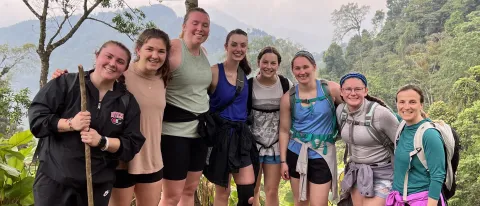 A group of students pose while on a hike in Guatemala; the forest is visible behind them