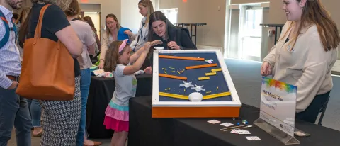 Students instruct a child how tp play with the marble run they built by hand