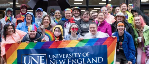 UNE community members gather with a UNE Pride banner in Monument Square in Portland