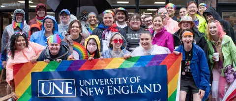 UNE community members gather with a UNE Pride banner in Monument Square in Portland