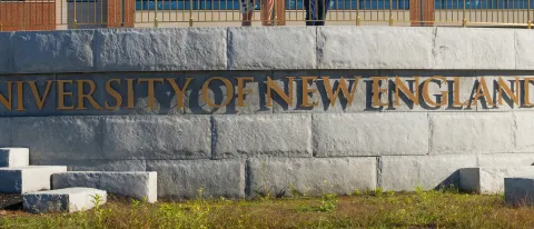 A metal sign against a brick wall reads "University of New England" 