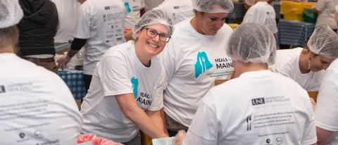 A volunteer smiles through the crowd of others helping to pack meal kits for the Meals for Maine event