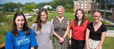 Four students who have received the Millennium Fellowship pose with Alethea Cariddi, associate director of sustainability at UNE, on a campus deck. The campus quad and commons are visible at back.