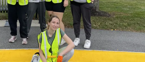 A group of students wearing yellow safety vests pose in front of the Westbrook Housing building displaying the painted sidewalk curbs they completed to enhance safety