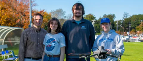 A faculty member and three students pose with a flying drone