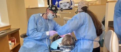 Two dental students clean a patient's teeth in the oral health clinic