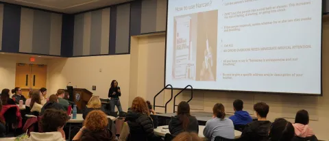 A woman presents a slide deck to a room of students