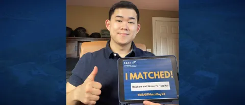 A man poses for a selfie holding a tablet displaying the words "I Matched!" while giving a thumbs up