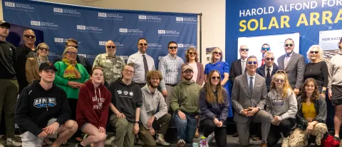 Members of UNE's Community pose in front of a mural inside the Alfond Forum