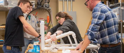 Three students and a professor assemble part of a wheelchair together