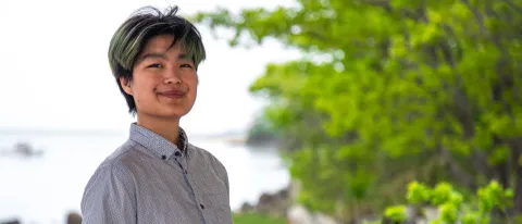 A UNE student poses in front of the Saco River on UNE's campus