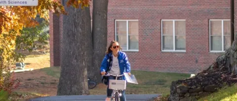 A UNE student bikes through campus in the fall 