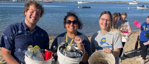 Three UNE students hold buckets of waste after cleaning up Freddy Beach