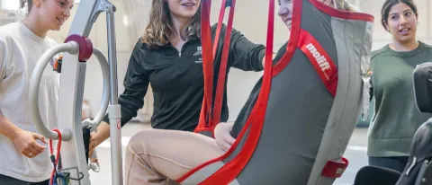 Students help a Maine Adaptive client into a power wheelchair using a lift