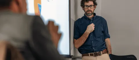 A UNE professor stands against a whiteboard while another professor speaks