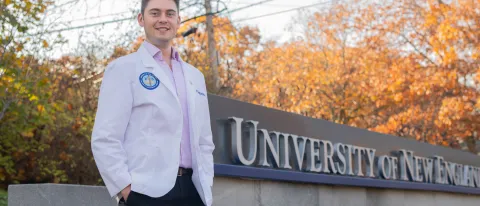 A UNE medical student poses in front of the University's entrance sign