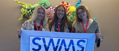 Three UNE researchers pose holding a Society for Women in Marine Science banner