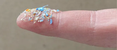 Photo showing a human finger holding small plastic fragments