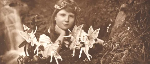 Sepia image of a girl in the woods surrounded by fairies