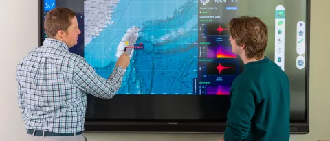 UNE Professor Will Kochtitzky displays a seismic activity map with a student