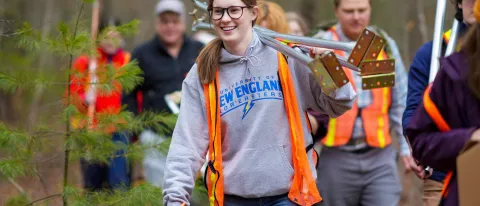 A UNE student carries research equipment through the woods