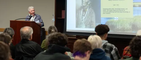 Poet Mikhu Paul speaks at a podium in UNE's St. Francis Room