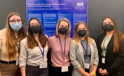Photo of four students and faculty member standing in front of a poster they presented at a conference in New York City