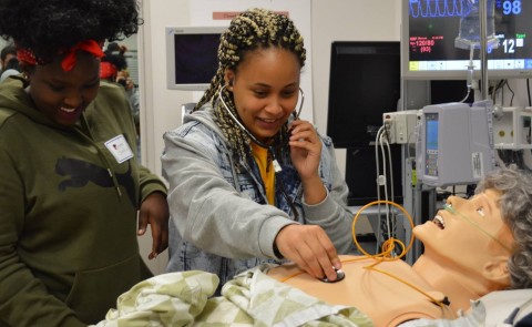 Two students practice using a stethoscope on a patient simulator mannequin