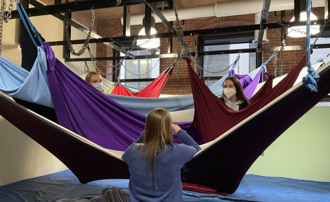 Two female students sit in a hanging tool for children at an occupational therapy clinic
