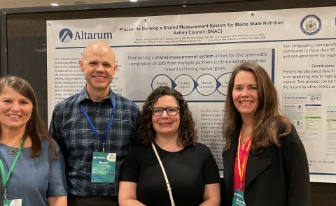 Four researchers pose in front of a poster at a conference. Lori Kaley (UNE) is far left.