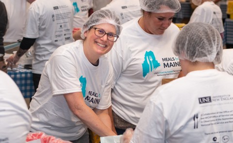 A volunteer smiles through the crowd of others helping to pack meal kits for the Meals for Maine event