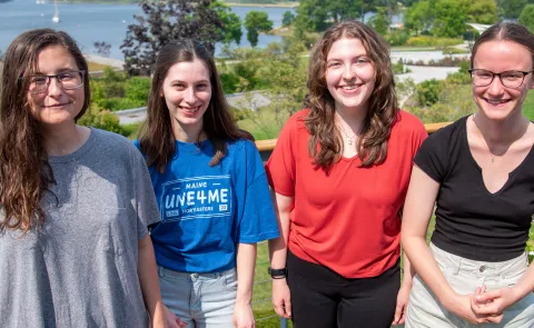 Four students who have received the Millennium Fellowship pose on a campus deck. The campus quad is visible at back
