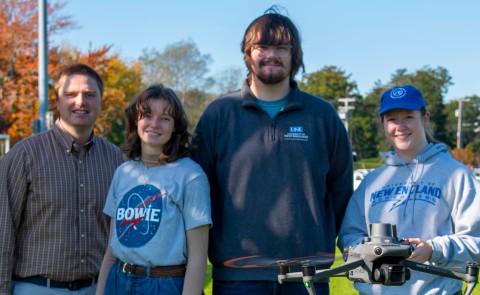 A faculty member and three students pose with a flying drone