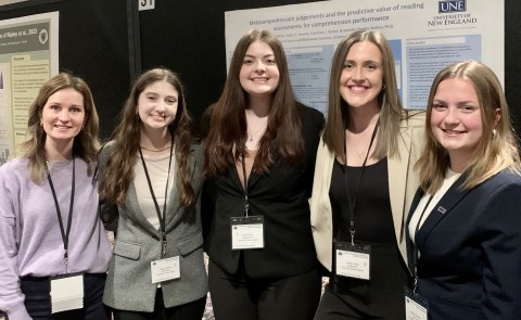 Four students and a professor pose in front of a research poster