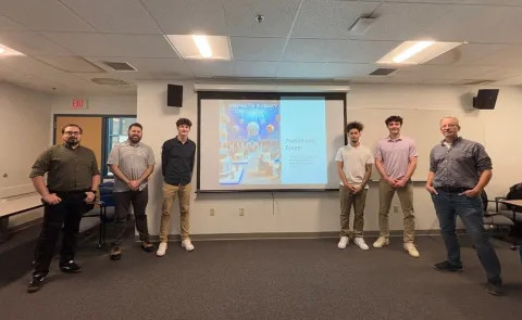 UNE students pose in front of a slideshow presentation with members of the DeepWater Buoyancy sales team