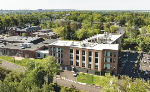 Aerial view of modern brick UNE health sciences campus building surrounded by trees and parking lots.