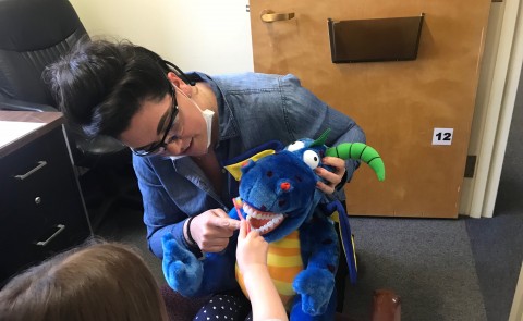 Dental student Ayla Nelson helps a young patient practice her toothbrushing skills using a stuffed animal