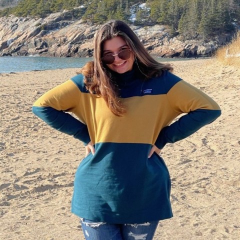 Zoe Henderson stands smiling on the sand at Sand Beach in Acadia National Park