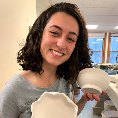 Olivia Scott stands smiling at the camera holding her handmade ceramics