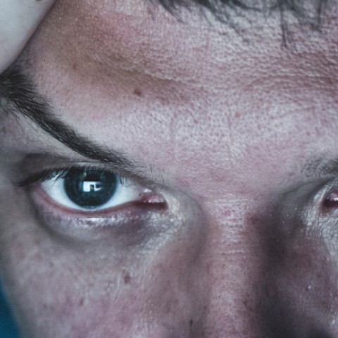 Image of man's eyes illuminated by computer screen, with pained expression.