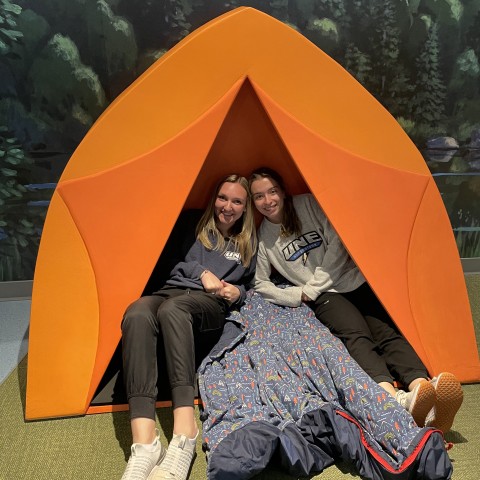 Two female students pose in an orange tent