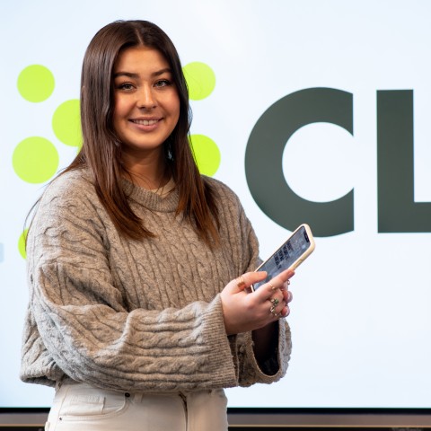 Abbie Anderson poses with a mobile phone. The name of her app, Clyk, is shown behind her