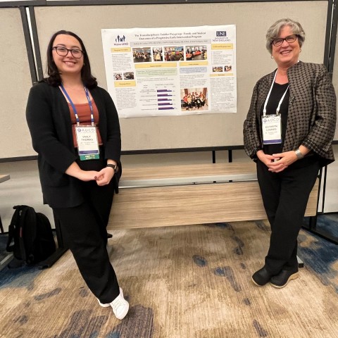 Photo of Emily Thomas and Kathryn Loukas posing in front of a research poster