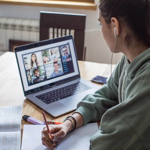 A young woman studying over a video call at a kitchen table
