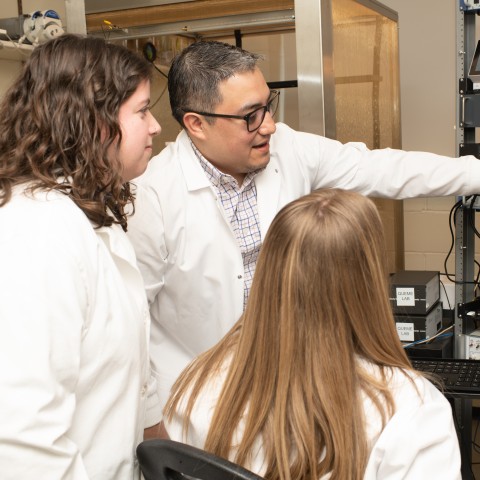 Three UNE researchers examine a microscope