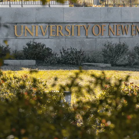 A stone sign bearing the name "University of New England" is seen through the trees