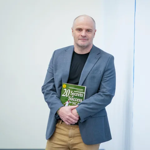 Photo of Norm O'Reilly against white background holding a book he has authored