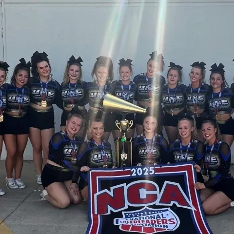 UNE cheer team members pose holding their championship trophy